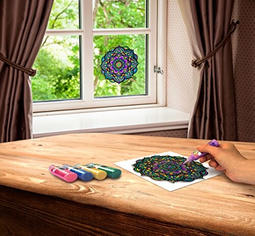 Hand coloring a mandala on paper with markers, window in background.